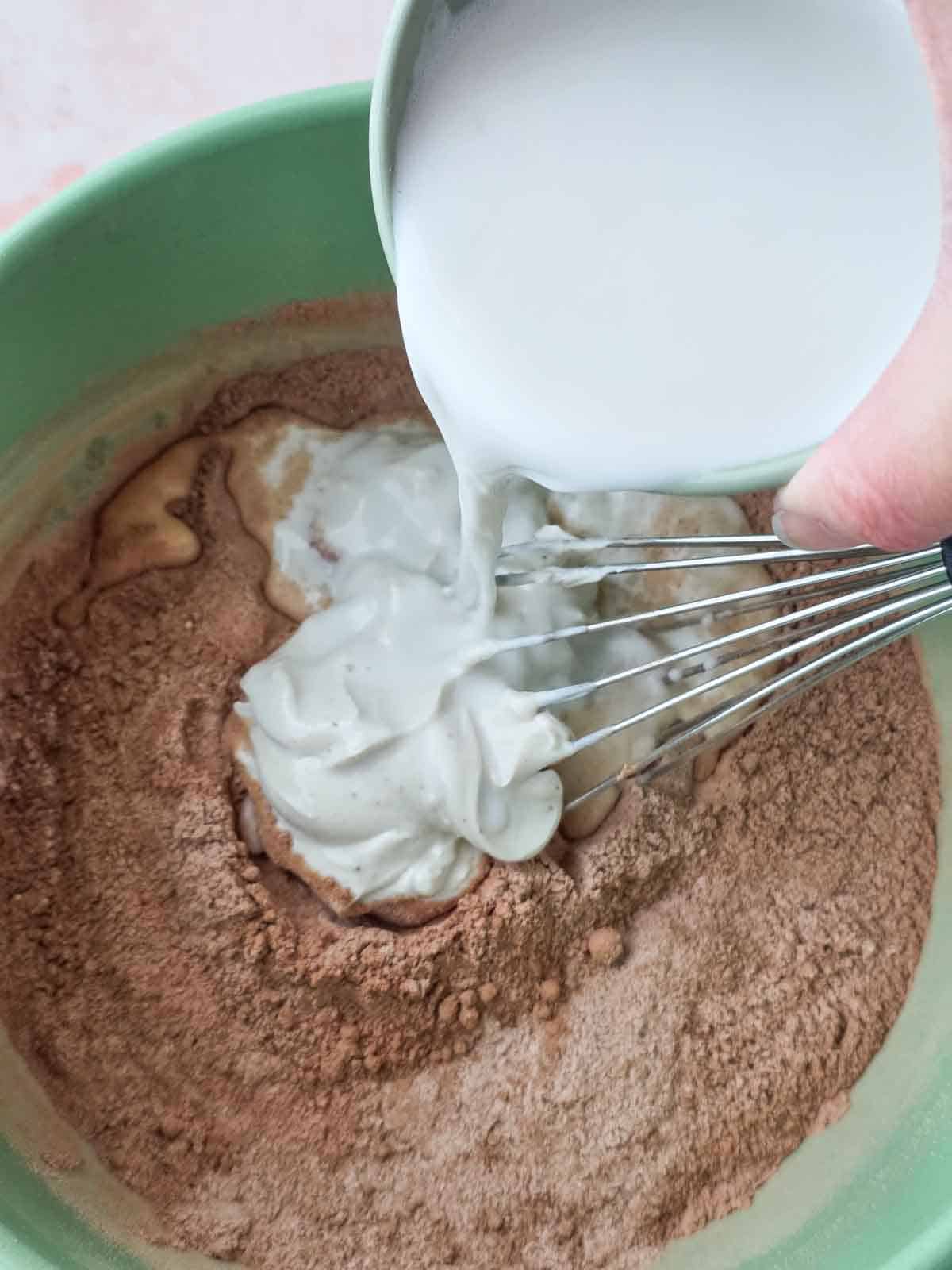 Plant milk being poured into the mixing bowl with yogurt and dry ingredients.