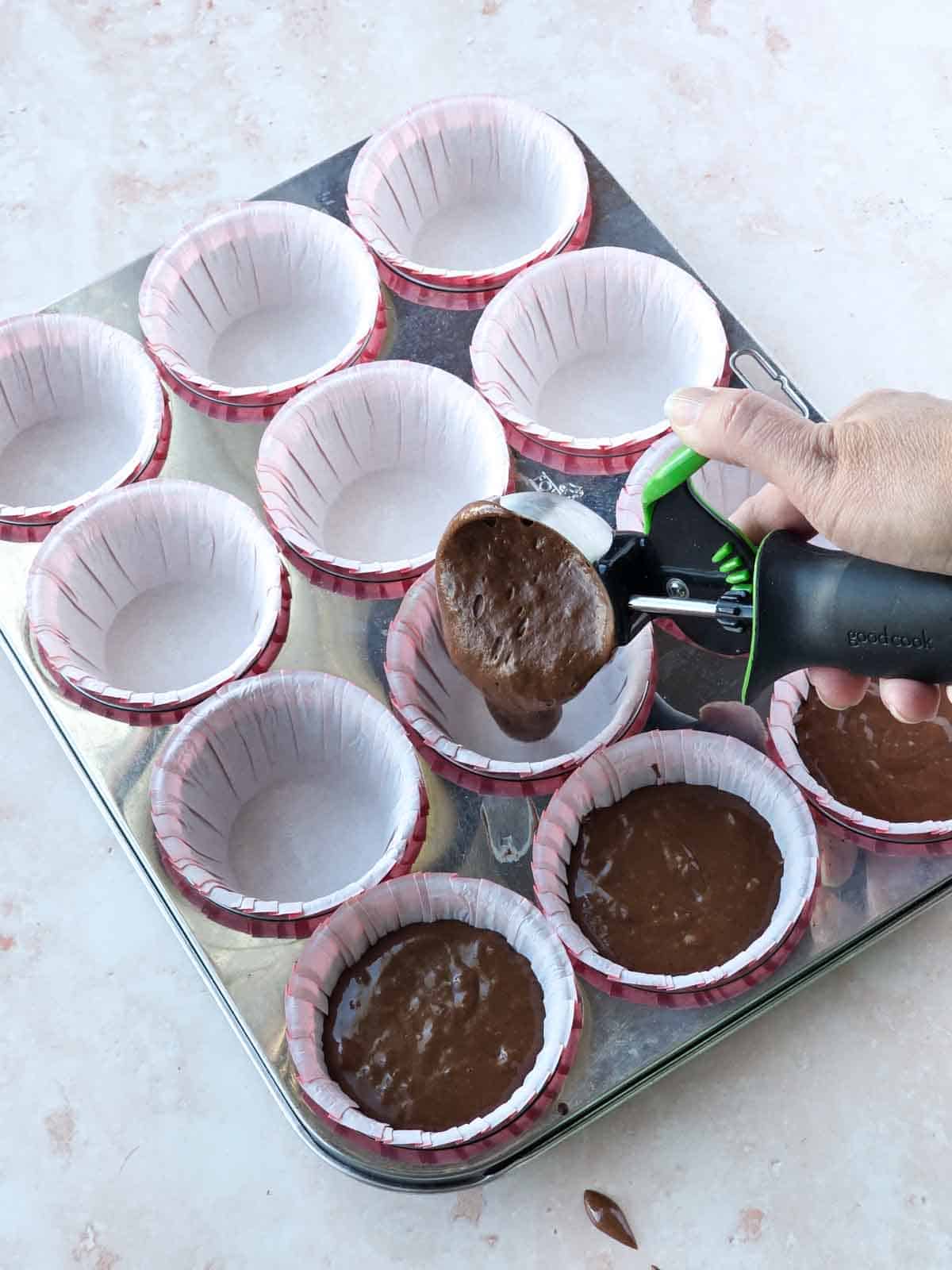 Scooping chocolate cupcake batter into lined muffin tin with a cookie scoop.
