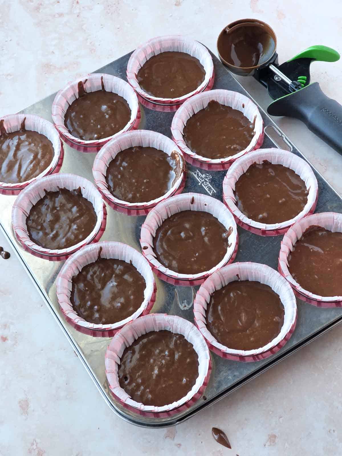 Cupcake batter portioned into paper liners in a muffin pan before baking.