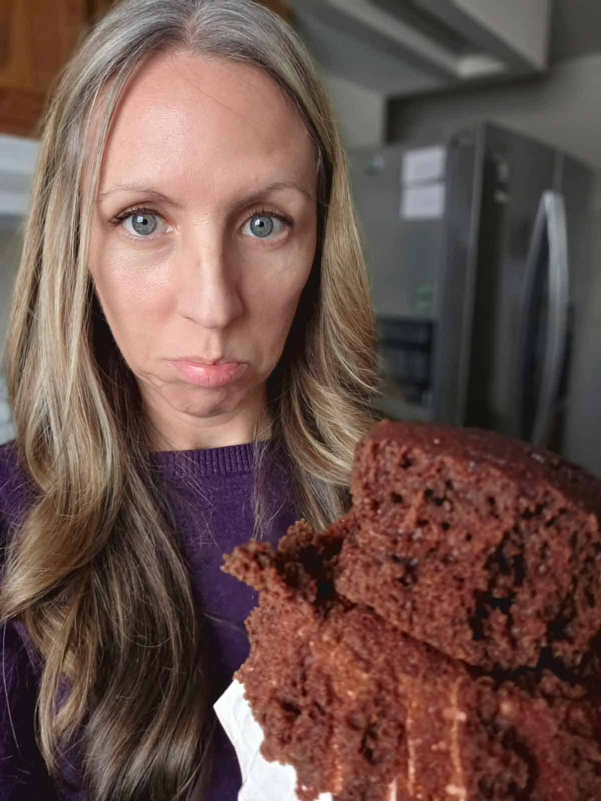Food blogger holding a broken vegan chocolate cupcake to show the soft crumb texture.