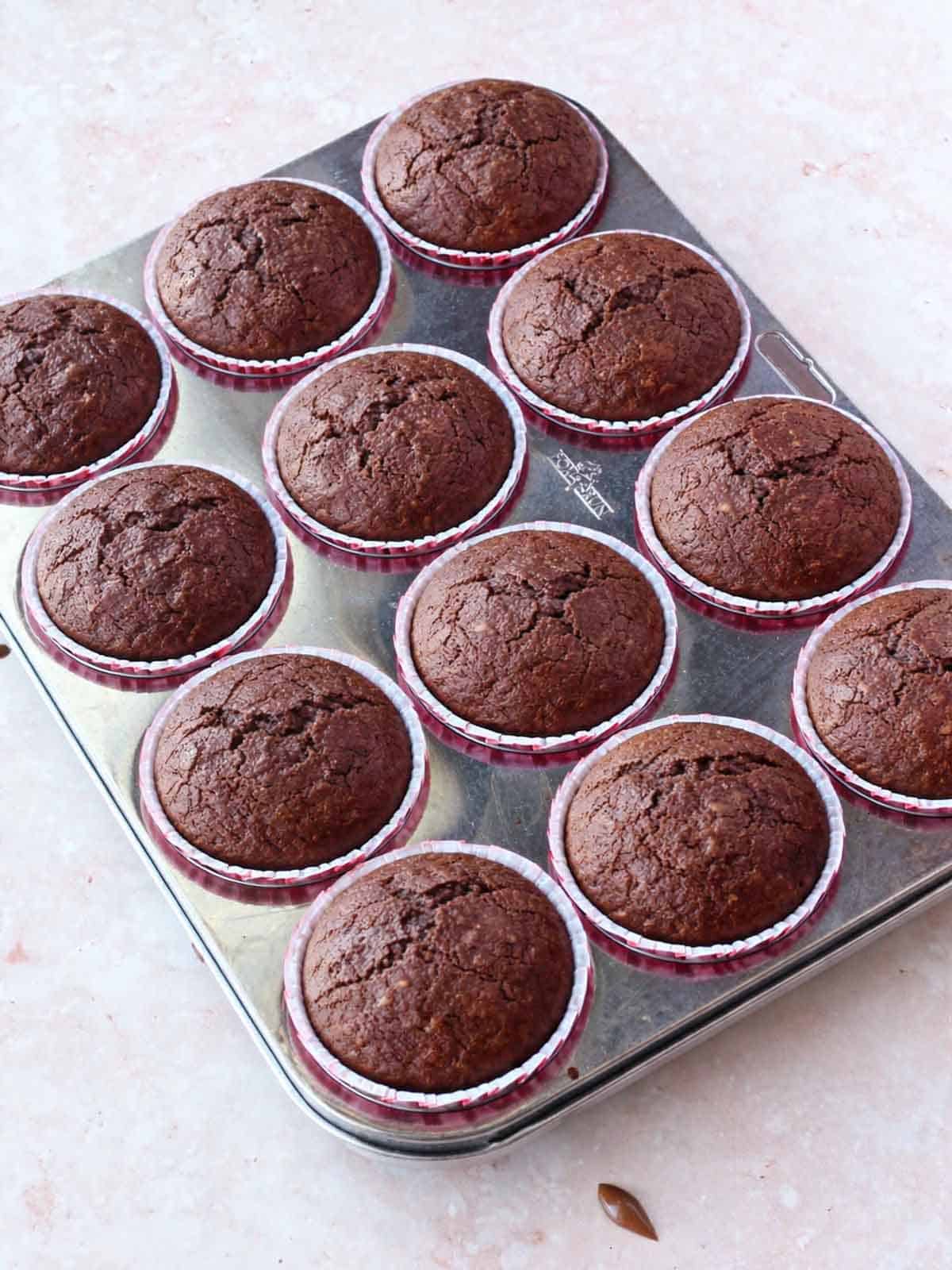 Fully baked chocolate cupcakes in a muffin tin.