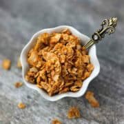 Crispy coconut bacon flakes in a small white bowl with a spoon, showing golden brown texture.