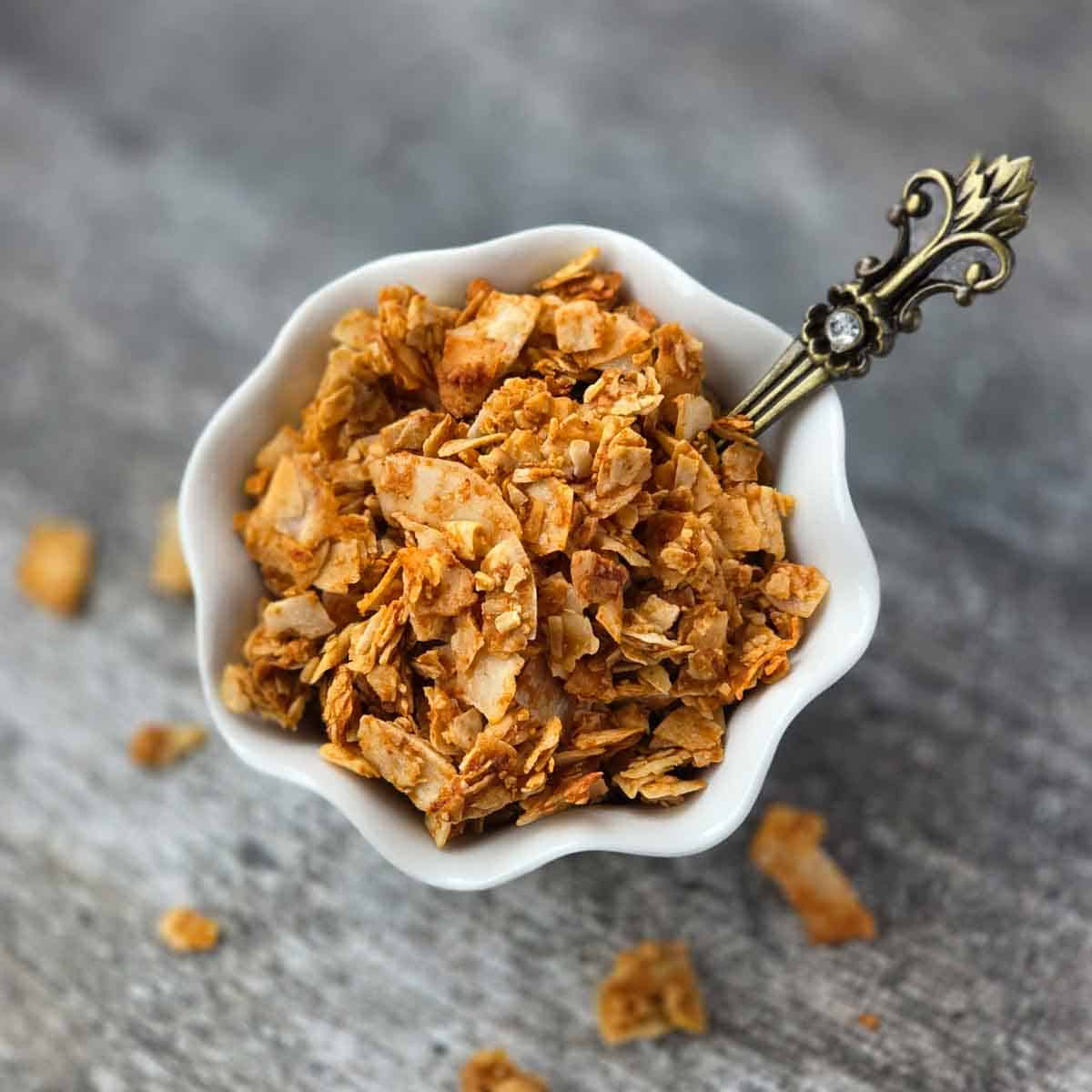 Crispy coconut bacon flakes in a small white bowl with a spoon, showing golden brown texture.