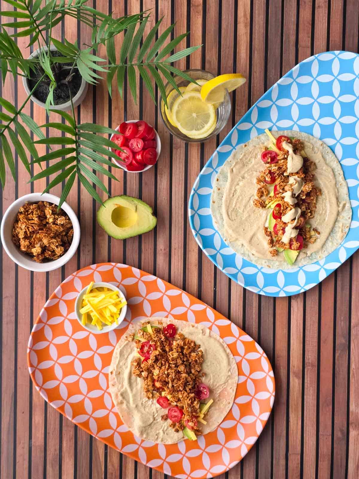 Two of the vegan BLT wraps topped with avocado, tomatoes, dairy-free cheese, coconut bacon, and ranch on colorful plates.