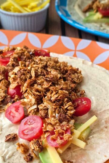 Detailed view of coconut bacon, tomatoes, and cheese layered over avocado and ranch on a soft tortilla.