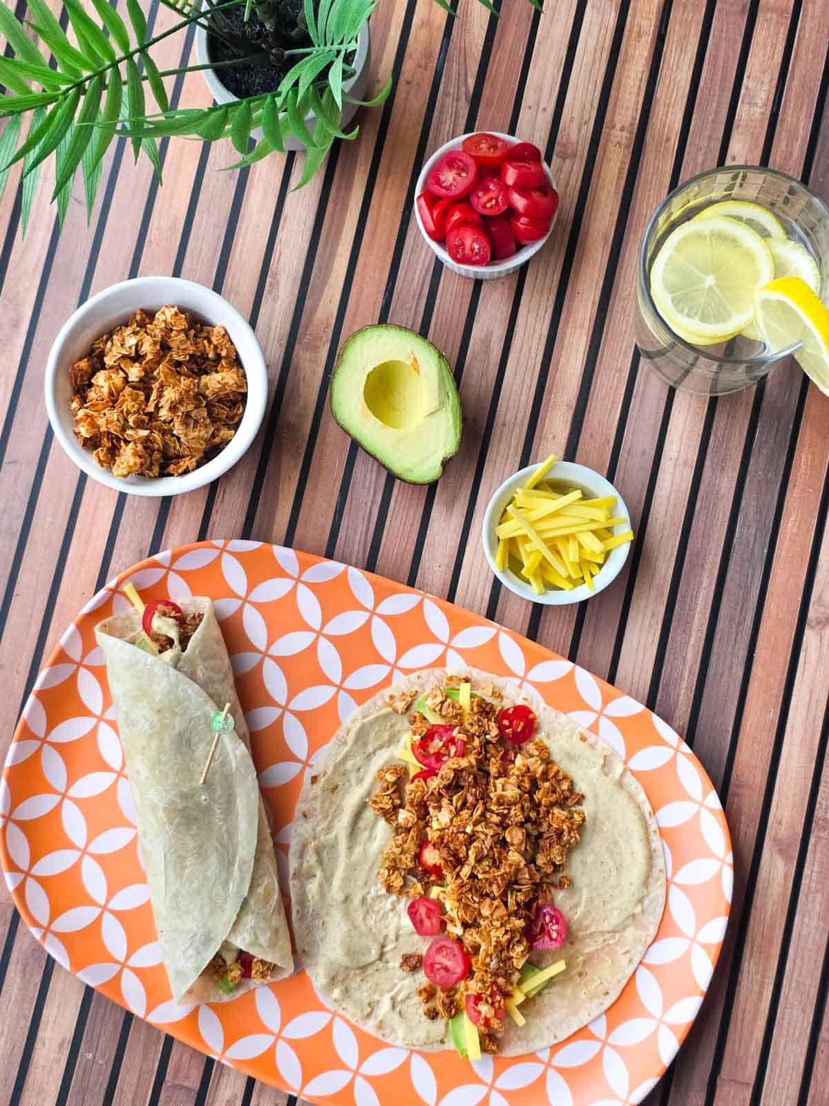 One folded tortilla wrap and one open wrap filled with plant-based toppings on a patterned plate.