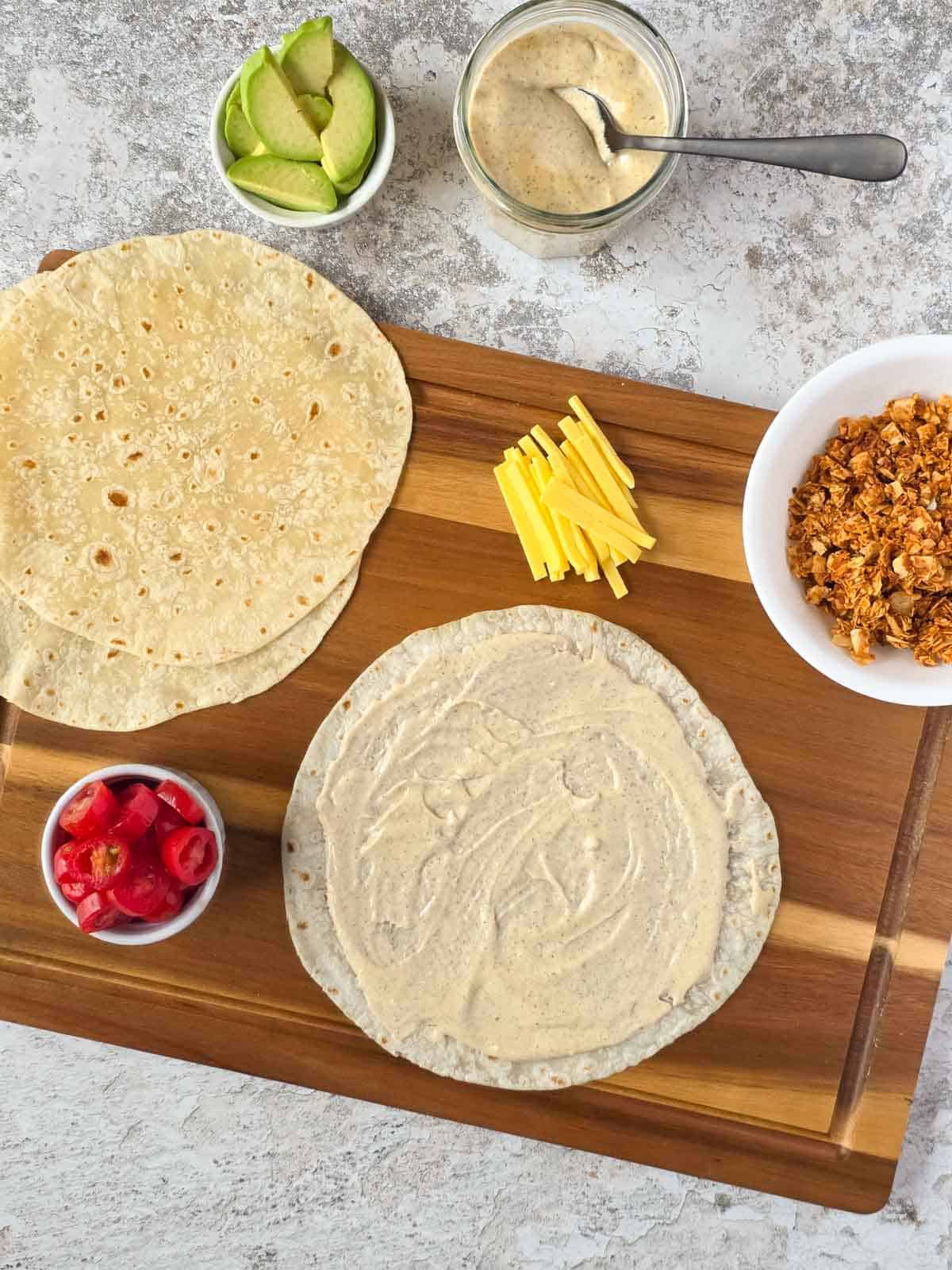 Tortilla spread with creamy dairy-free ranch dressing on a wooden board.