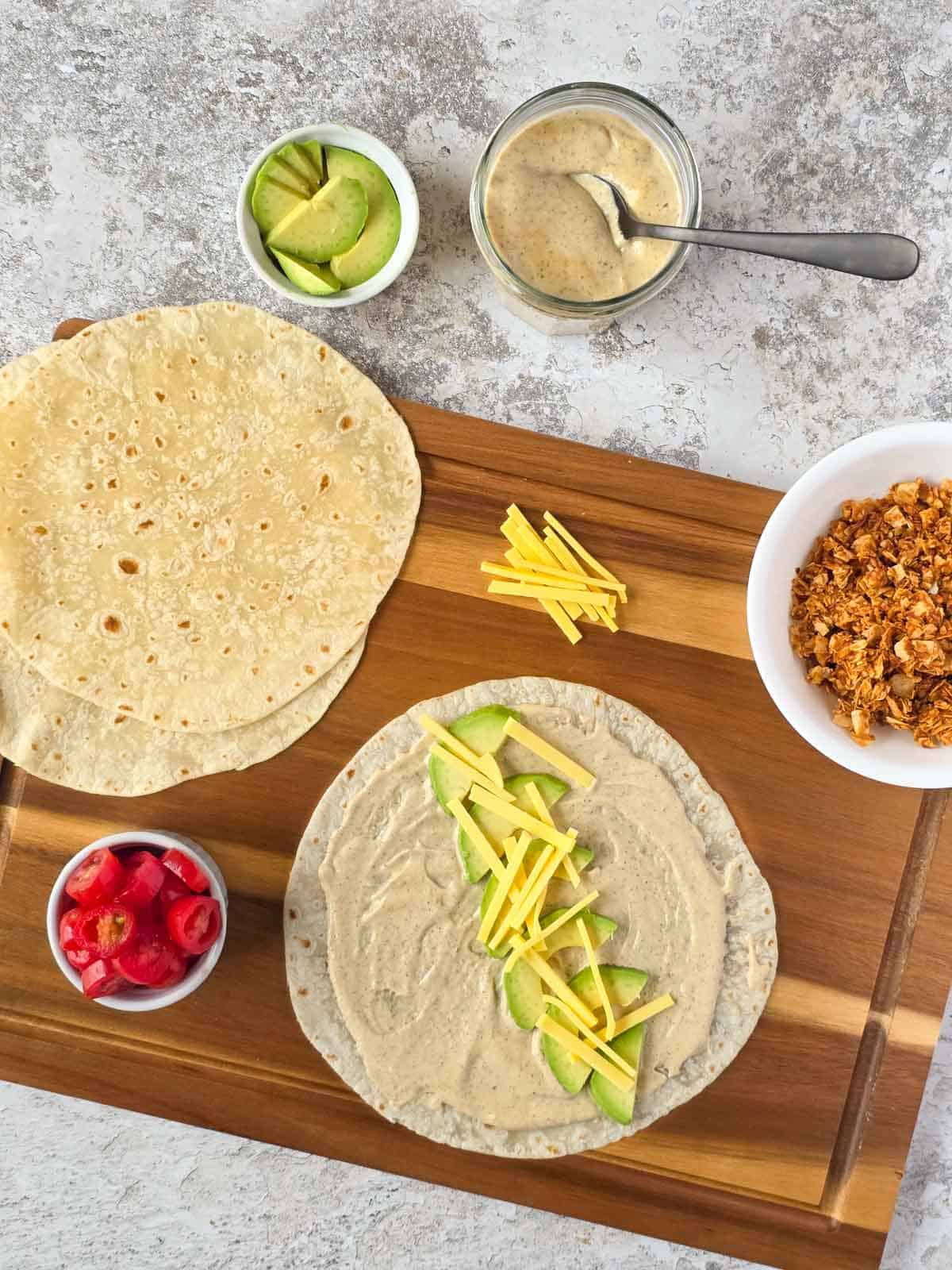 Dairy-free cheese added on top of avocado and ranch in a tortilla shows how vegan BLT wraps are assembled step by step.