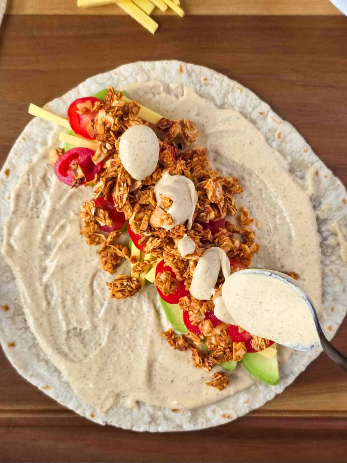 Close-up of creamy vegan ranch being drizzled over coconut bacon and vegetables.