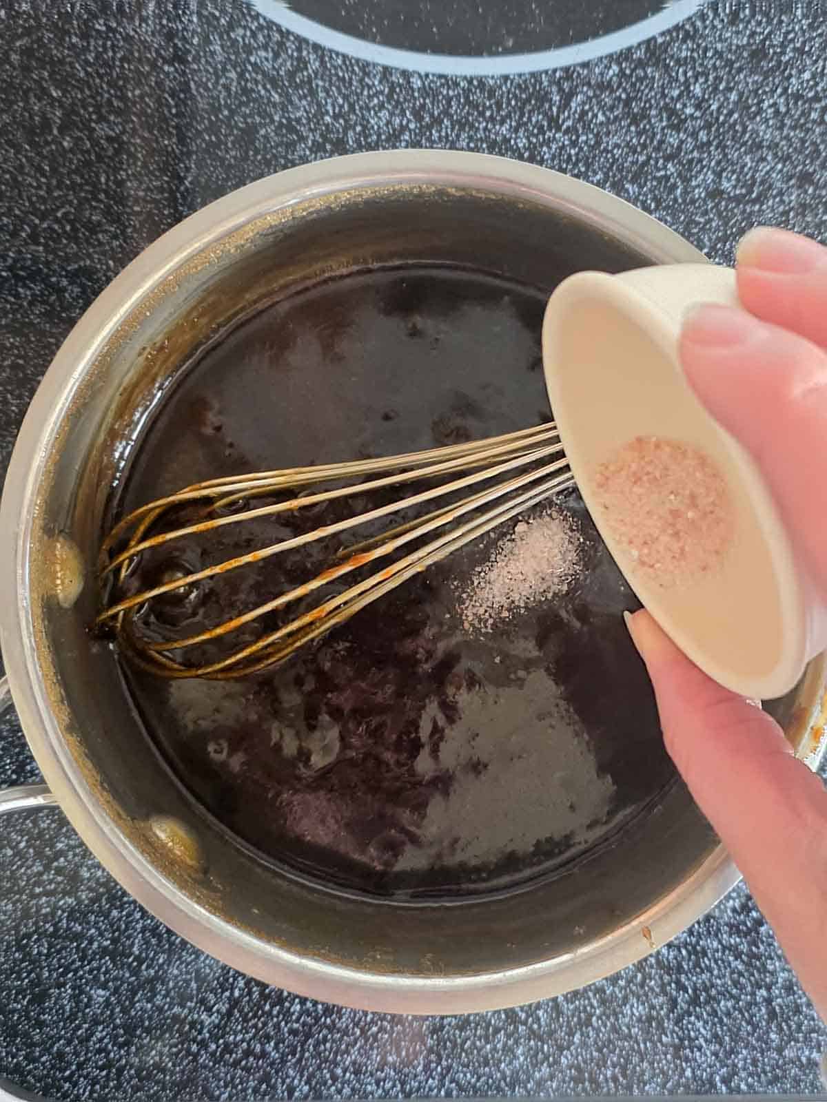 Salt being poured into the finished caramel sauce in the pan.