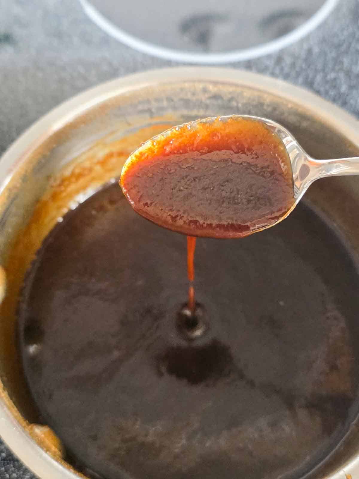 A spoon dripping caramel sauce into the pan to show that it is thinner when it first finishes cooking.