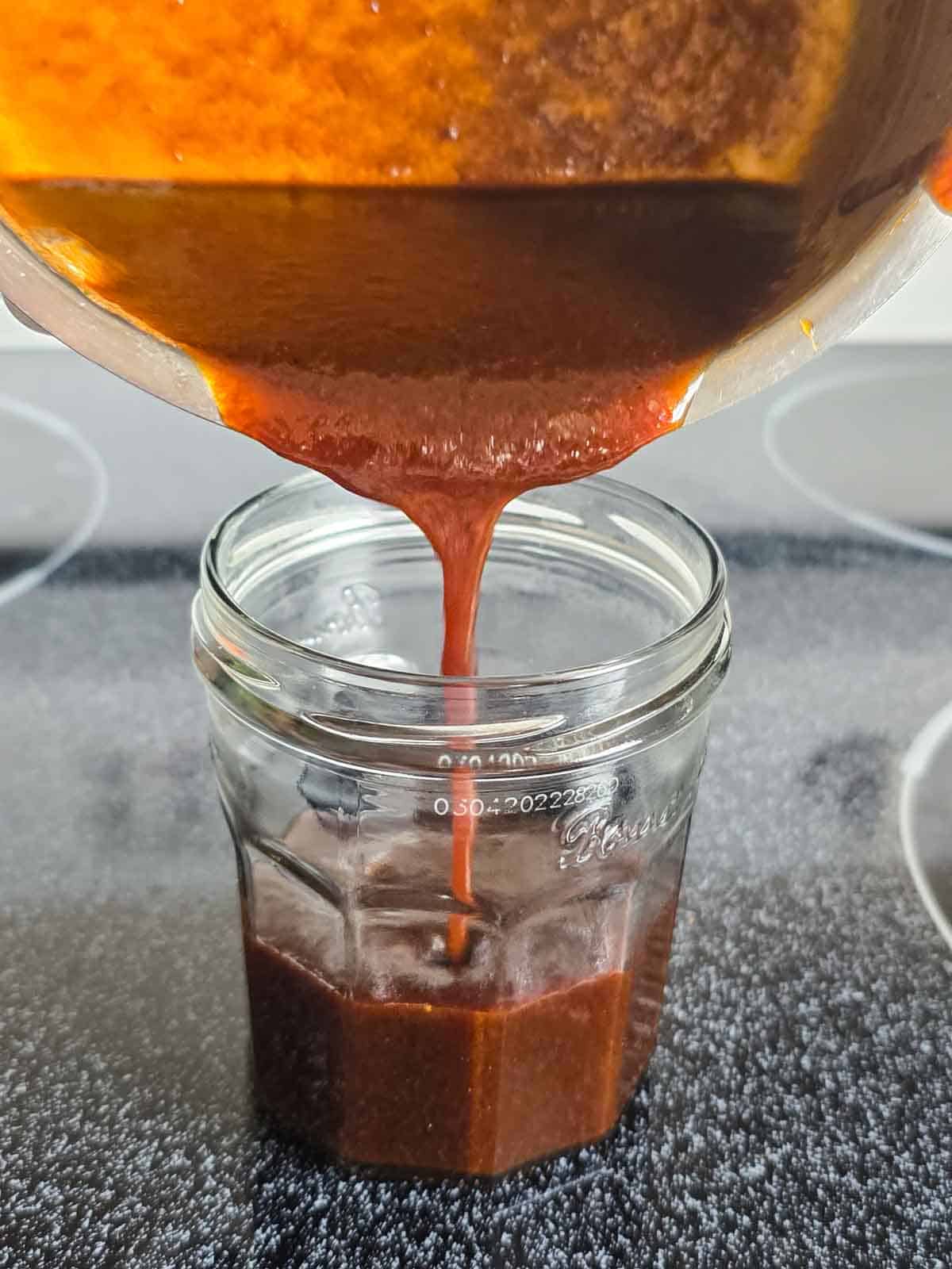 Finished vegan salted caramel sauce being poured into a glass jar.