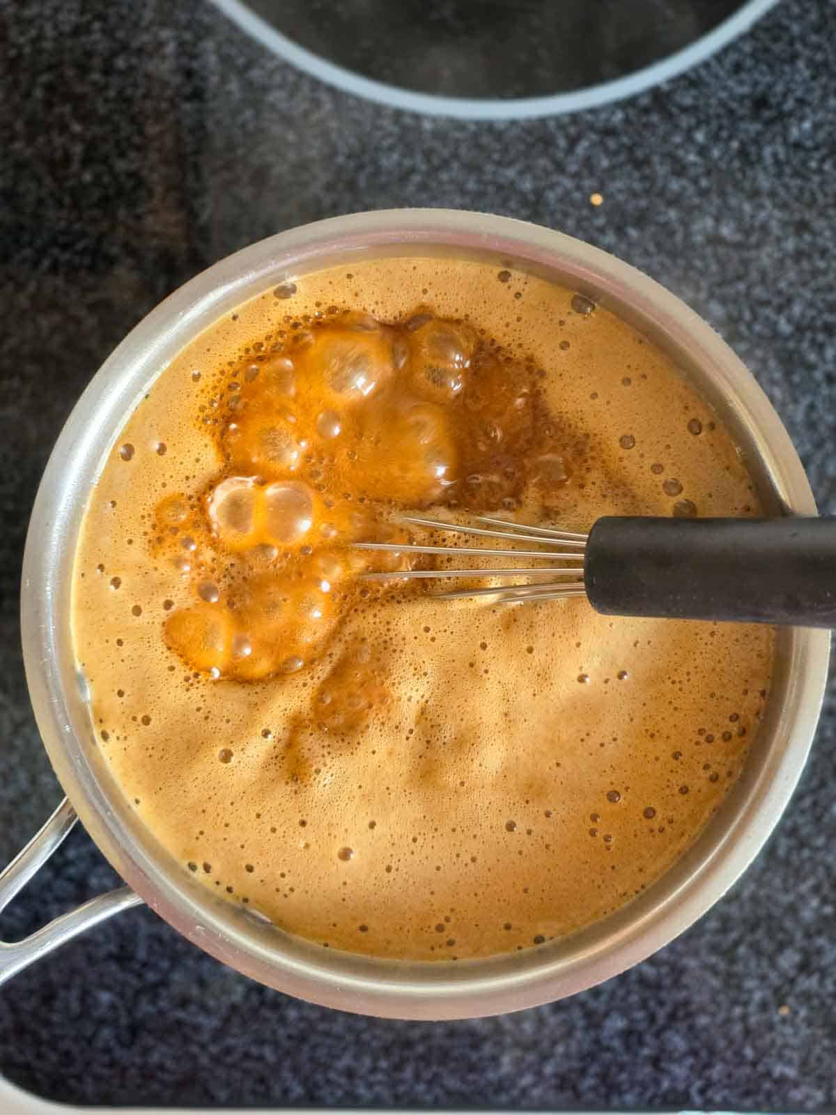 Coconut sugar and coconut milk shown at a low boil on the stove before being reduced to a simmer.