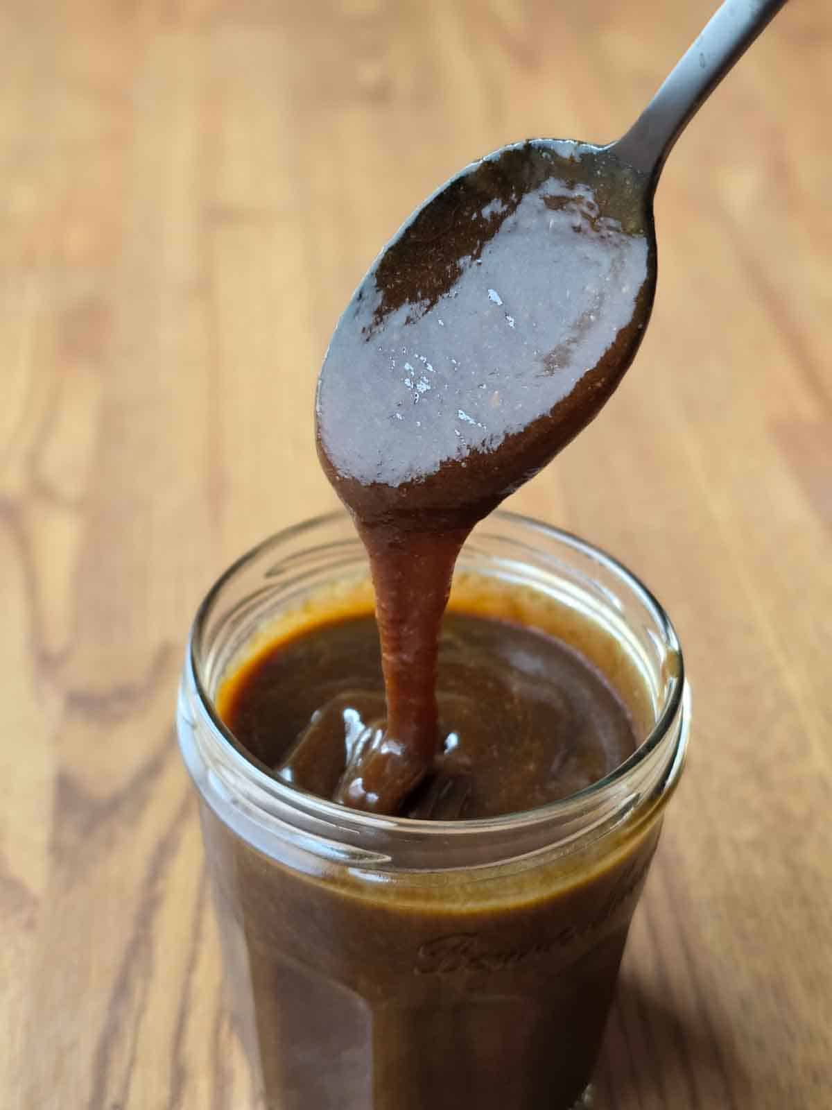 A spoon dripping thickened caramel sauce into a jar to show consistency after being refrigerated overnight.