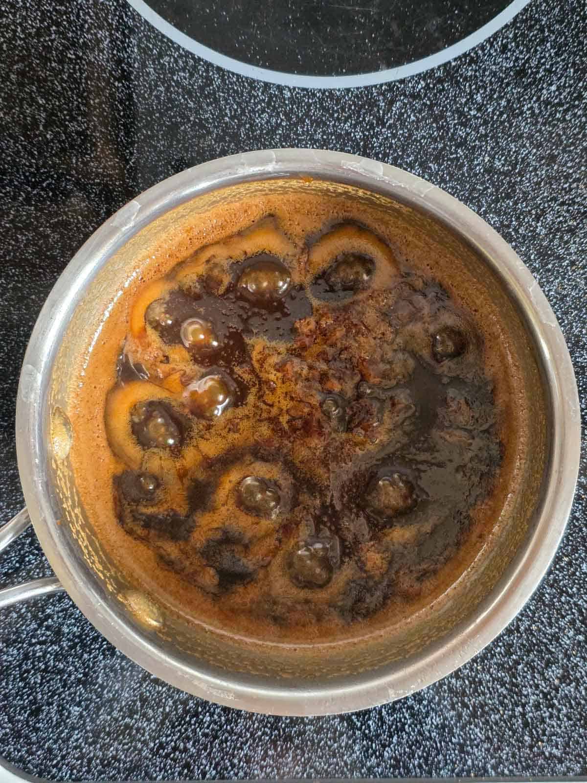 A pan of caramel sauce shown at a low simmer with only a few bubbles on the surface.