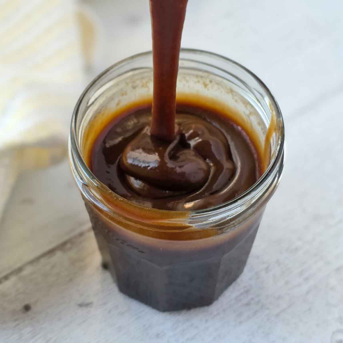 Thick, rich, vegan caramel sauce being dripped from a spoon to show texture.