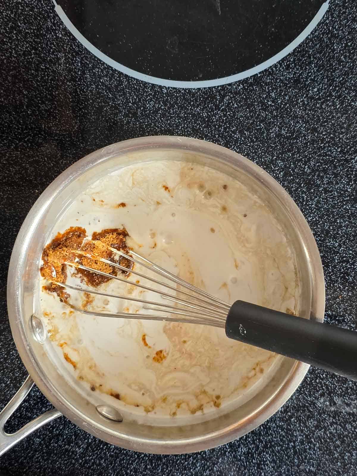 A whisk in a pan combining coconut milk and coconut sugar.