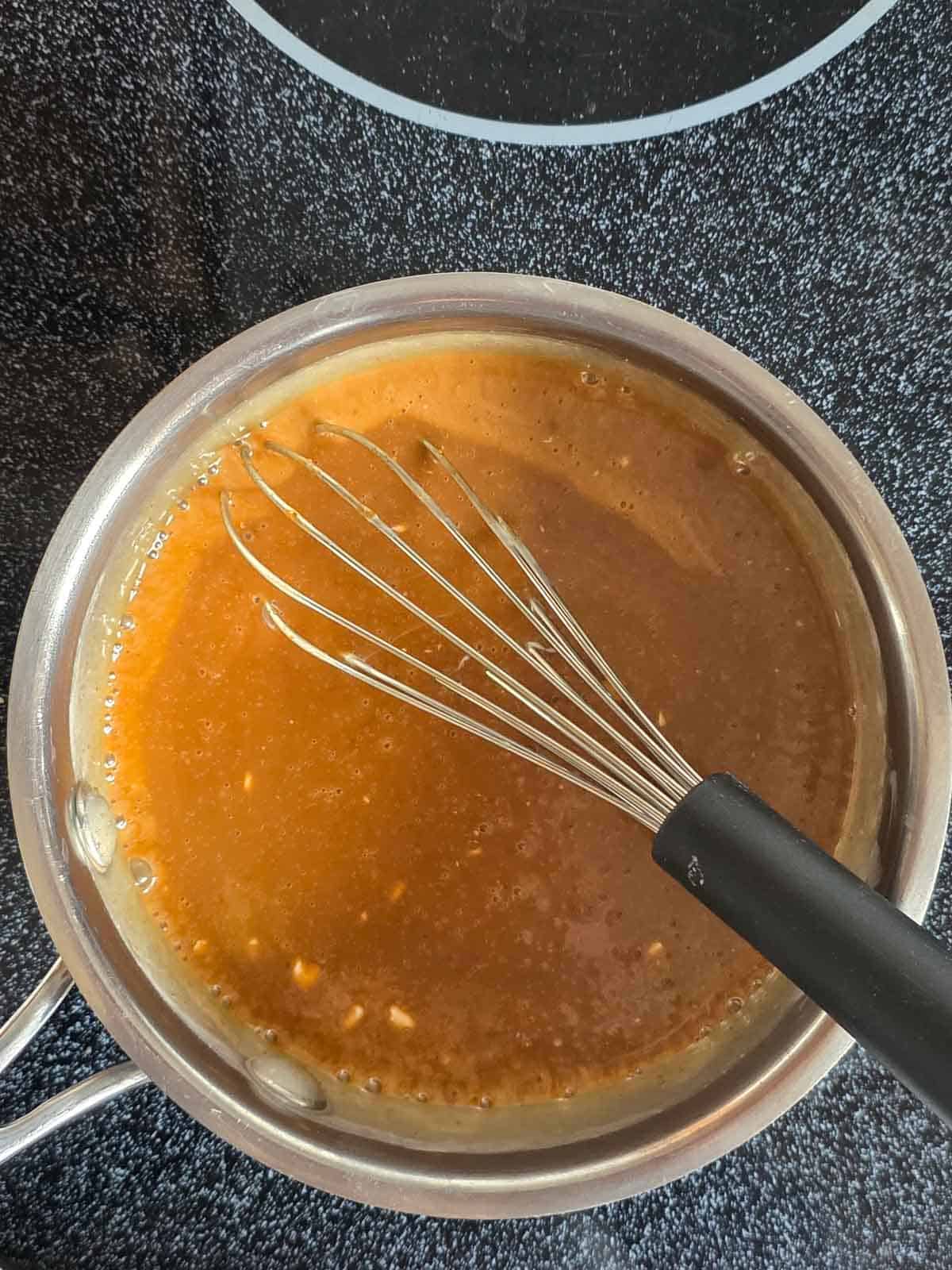 A smooth golden caramel sauce in a pan with a whisk ready to start cooking.