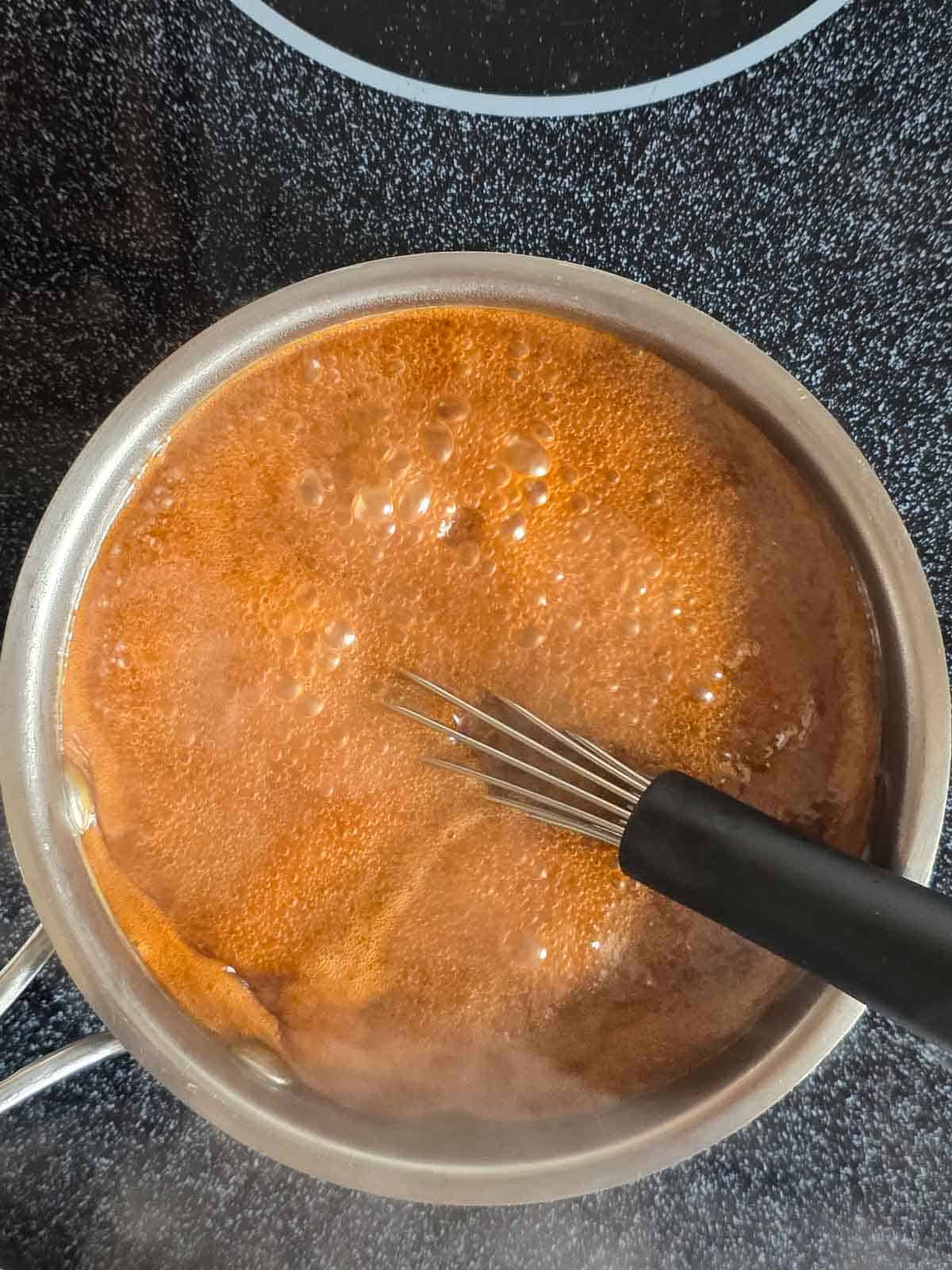 A pan of coconut sugar and coconut milk bubbling away while being whisked.