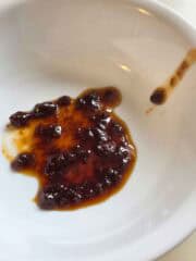 Caramel sauce that has separated being shown in a white bowl to show texture.