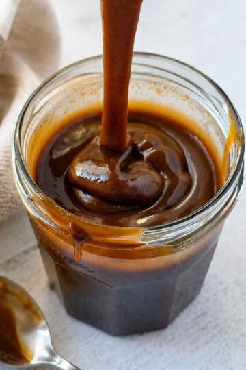Thick, rich, vegan caramel sauce being dripped from a spoon to show texture.