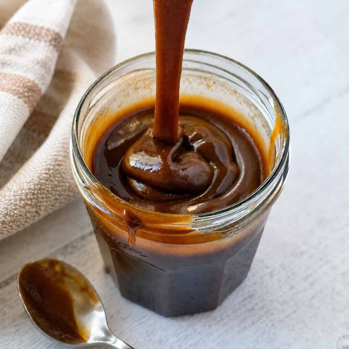 Thick, rich, vegan caramel sauce being dripped from a spoon to show texture.