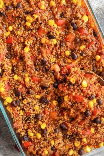 Vegan enchilada bake with corn, black beans, tomatoes, and enchilada sauce being scooped up by a large serving spoon.
