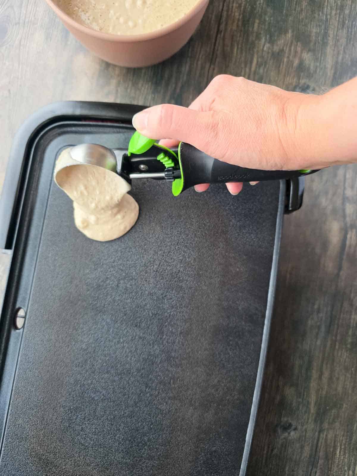 Scooping pancake batter onto a preheated griddle.