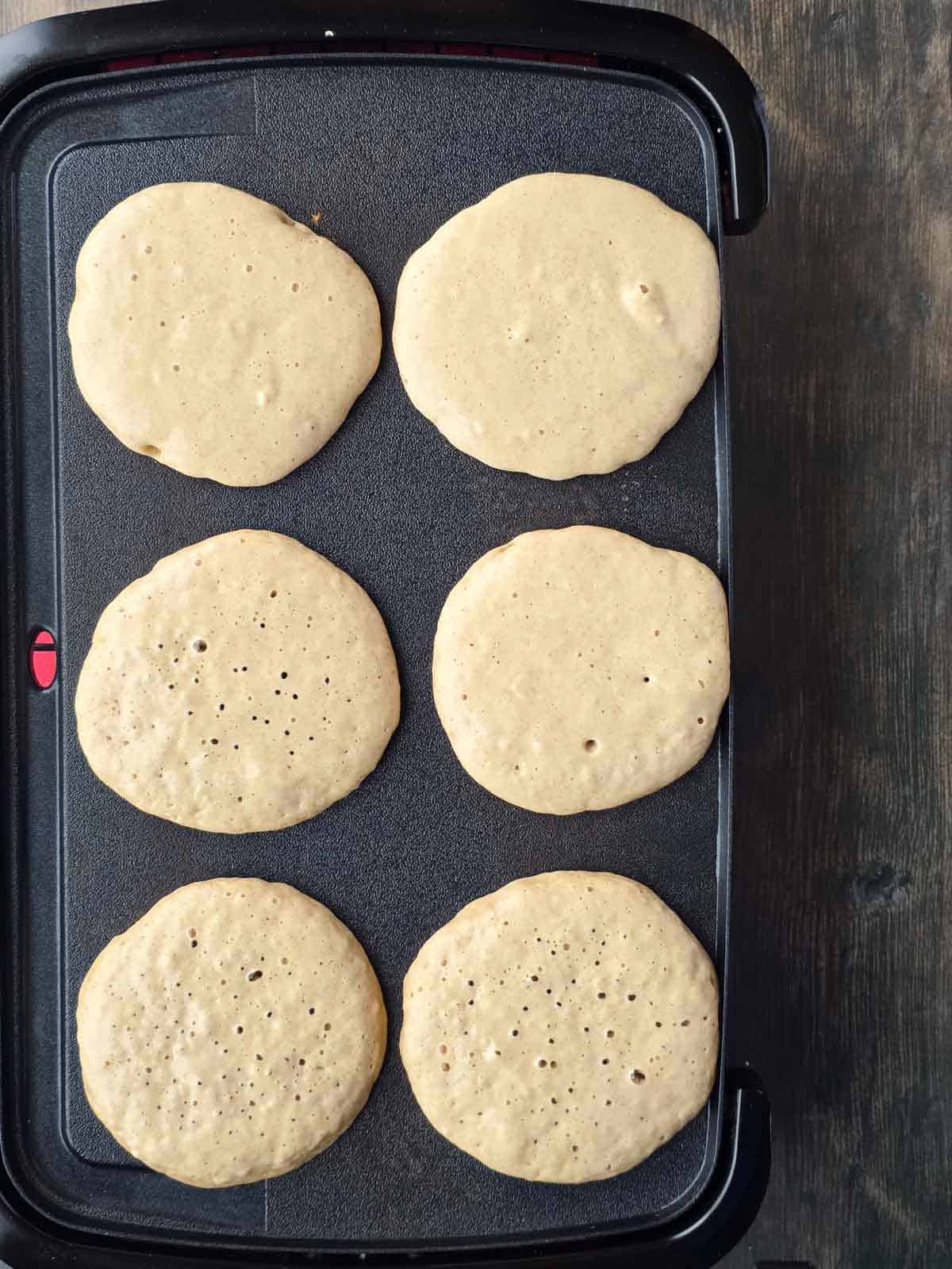 Pancakes cooking on a griddle with bubbles forming on top.