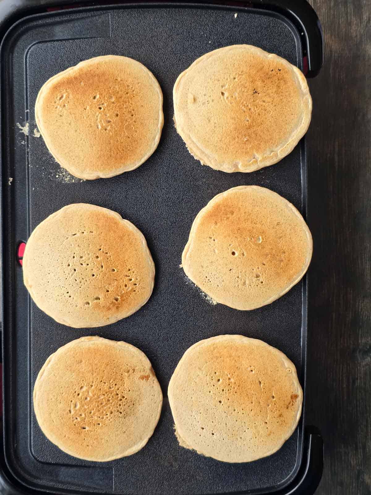 Golden brown pancakes cooking evenly on a griddle.