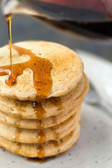 Stack of homemade pancakes with maple syrup being poured on top.