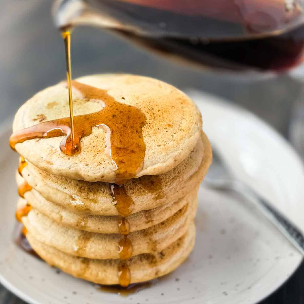 Stack of vegan thick and fluffy pancakes with maple syrup being poured on top.