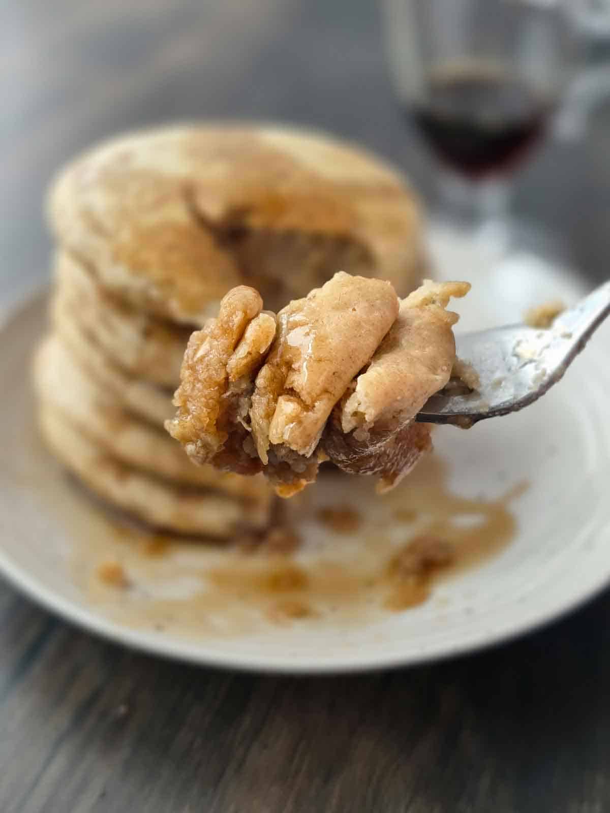 Fork lifting a bite of thick and fluffy pancakes with syrup on them.