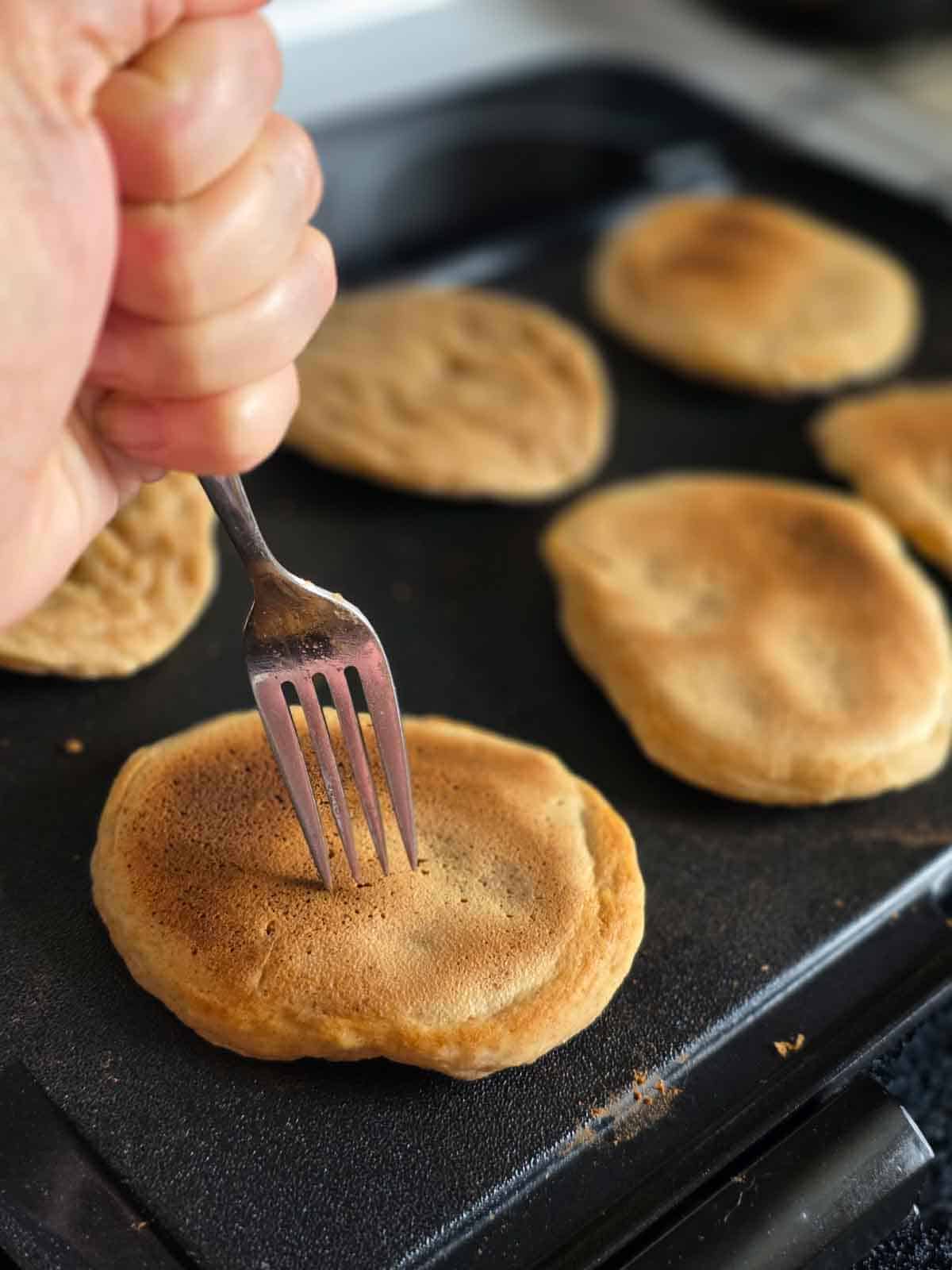 Checking pancake doneness with a fork on a griddle for pancakes that cooked too long.