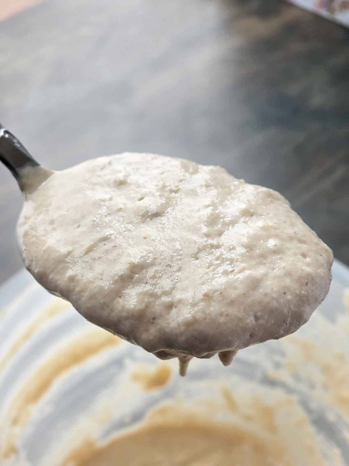 Thick pancake batter resting on a spoon to show texture of what makes thick and fluffy pancakes.