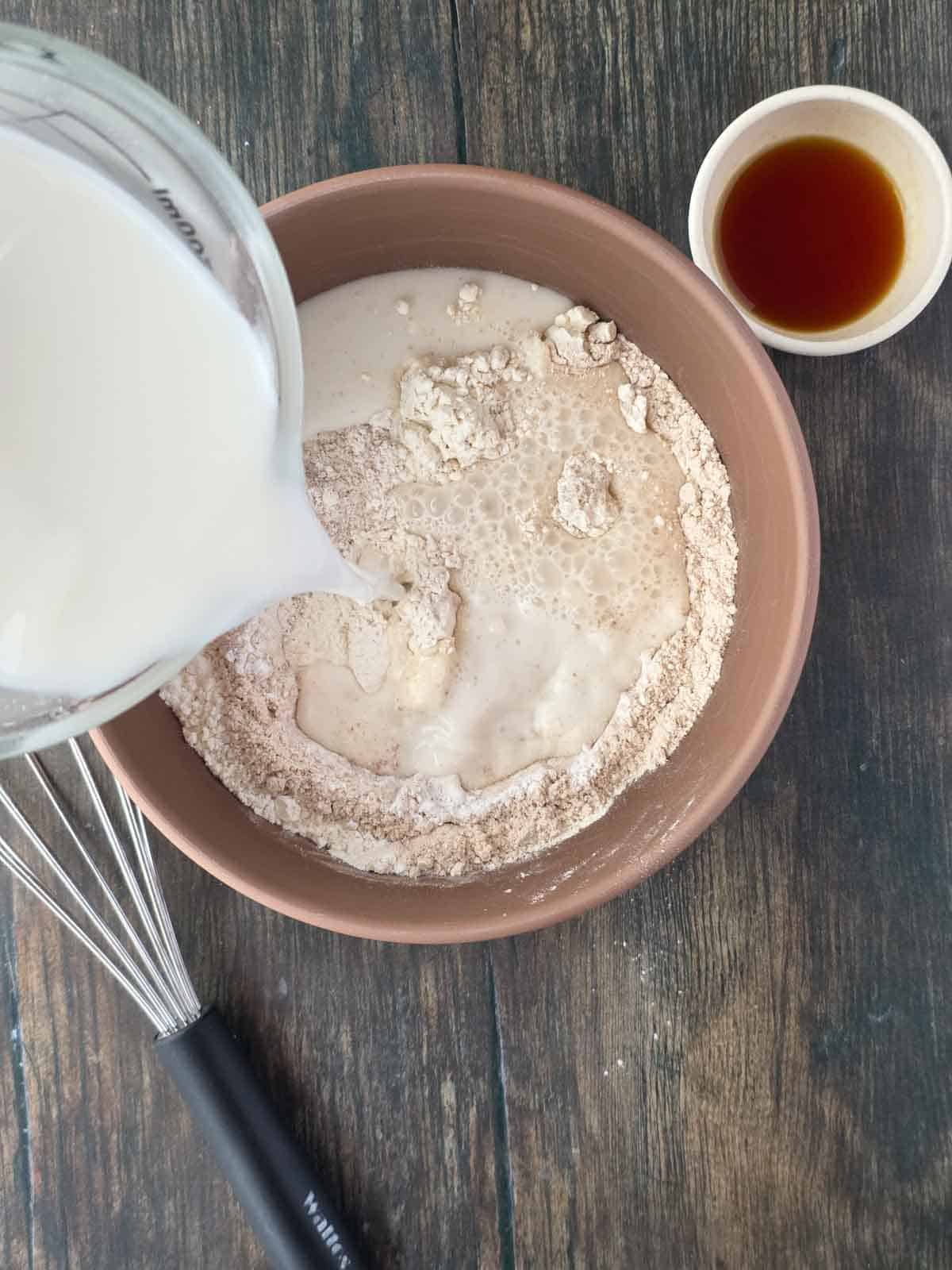 Pouring plant milk into the pancake batter mixture.