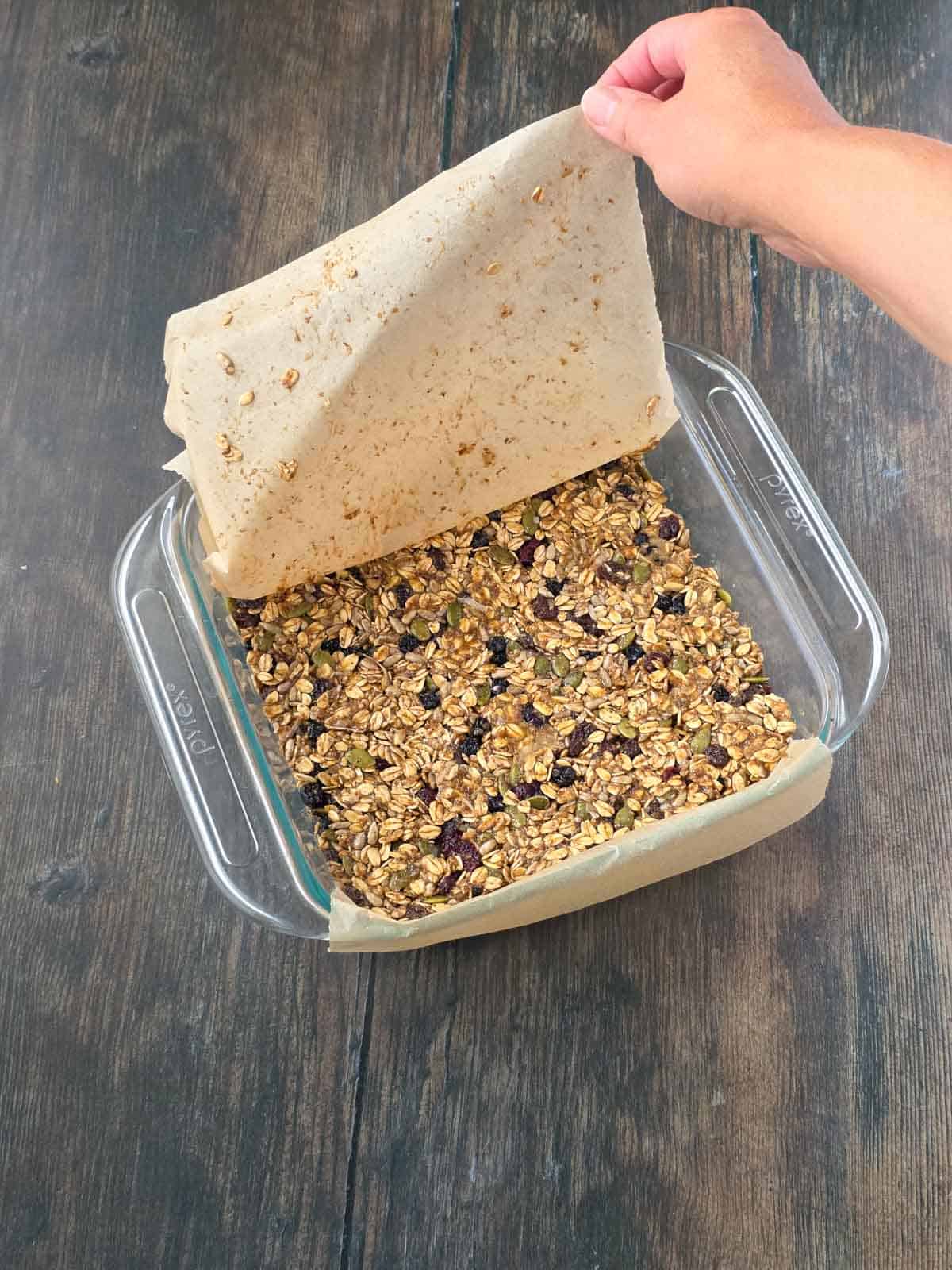 Removing the parchment paper after firmly pressing the triple berry granola bar mixture into the pan.